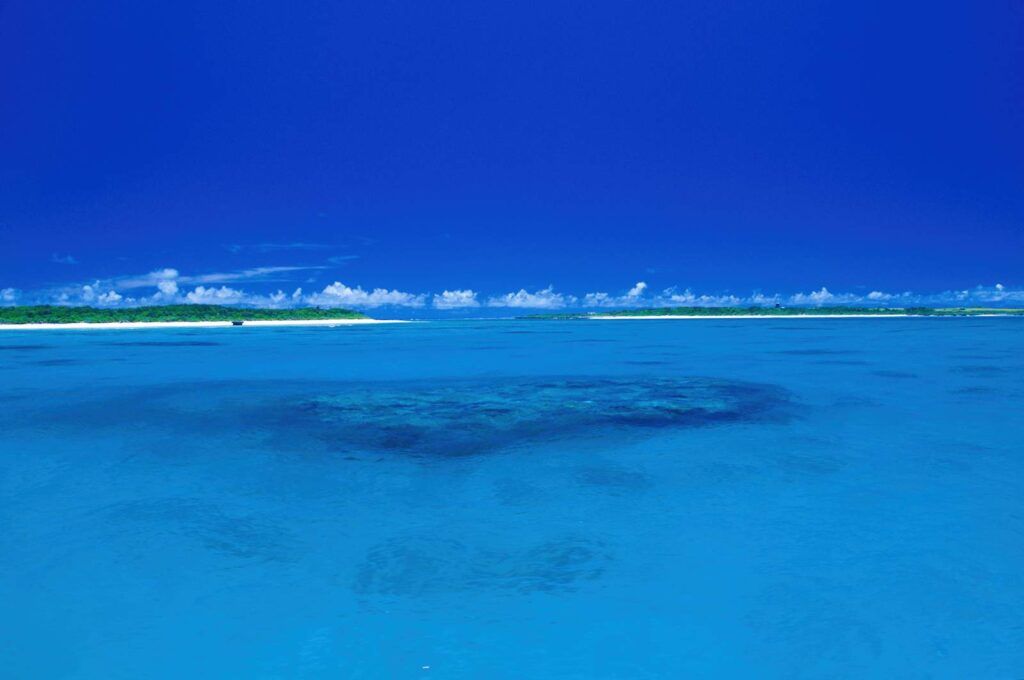 鮮やかな青い海と、遠くに島と白い雲が広がる水平線。