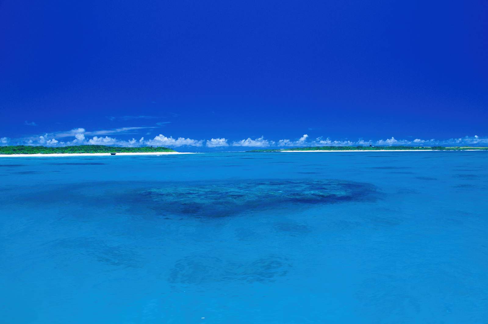 鮮やかな青い海と、遠くに島と白い雲が広がる水平線。